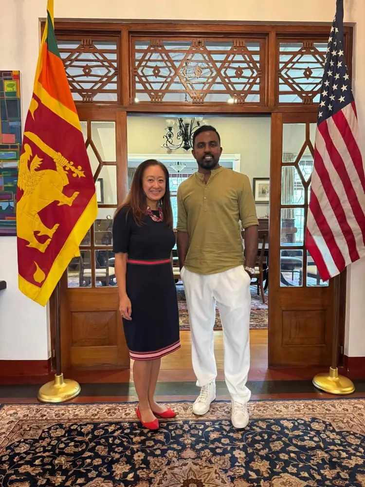 Sanjeewa and Julie Chung photographed between Sri Lankan and U.S. flags.